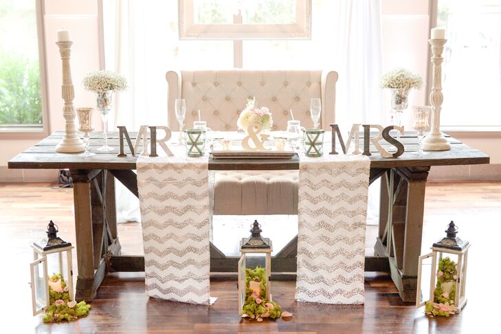 Brittney and Josh's sweetheart table embodied shabby chic: They sat in an oversize ivory lounge chair pulled up to their rustic wooden farm table, draped with copper chevron runners and a wooden "Mr. & Mrs." Vintage candelabras and lanterns overflowing with moss and blush petals softened the setting.