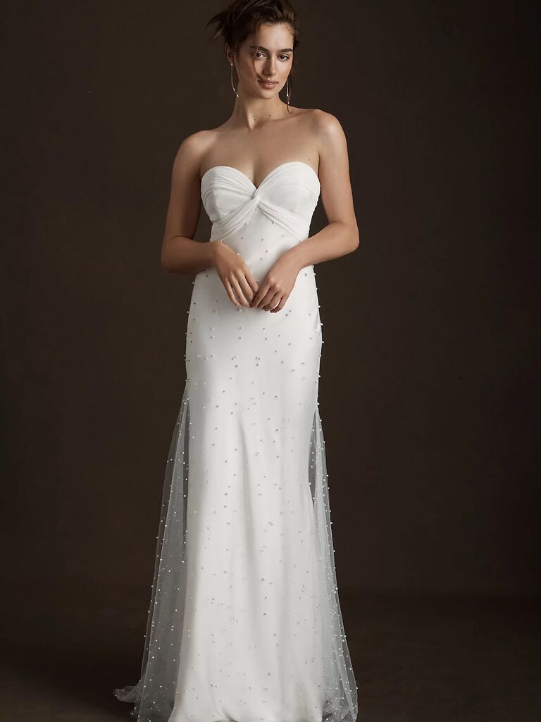 Model wears a white strapless dress embellished with jewels. 