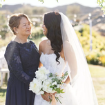 A bride and mother of the bride smile at each other.