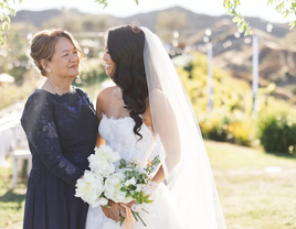 A bride and mother of the bride smile at each other.