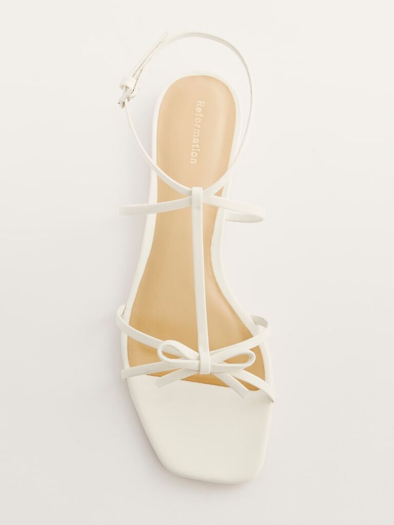 White flat sandal with slim ankle straps and a sleek bow