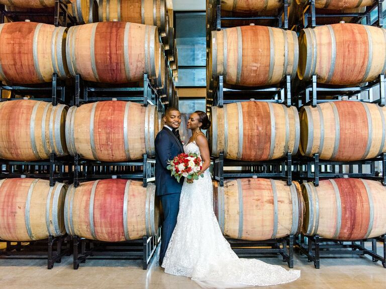 Bride and groom posing in front of wine barrels. 