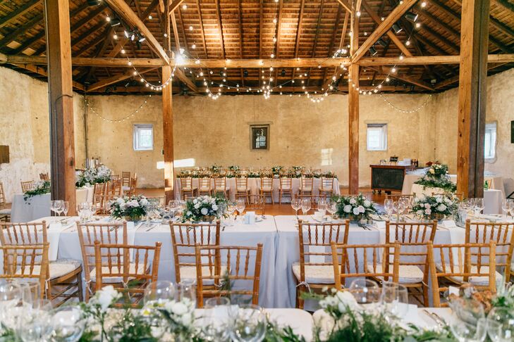 Inside the grounds' 19th-century stone barn, several large farm tables were arranged under romantic string lights. A number of floral arrangements featuring greenery and white roses lined each table.