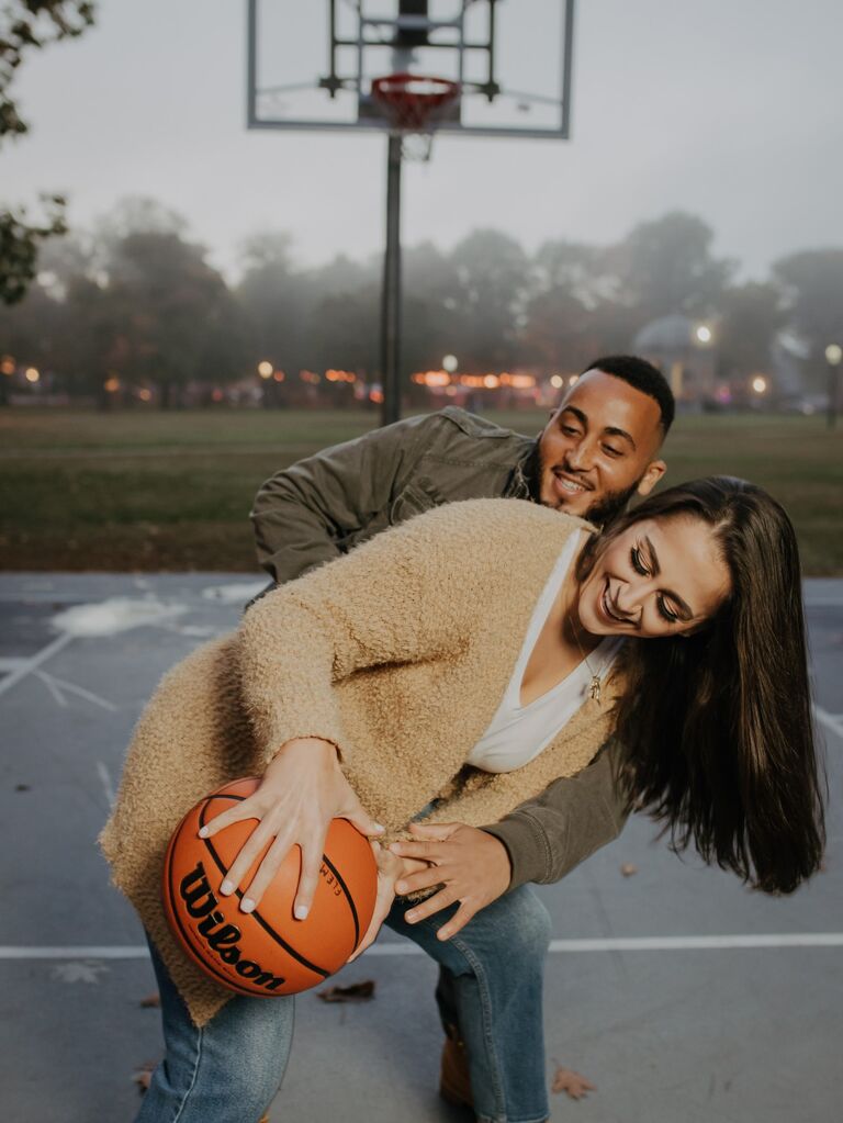 Couple plays basketball while posing for the camera. 