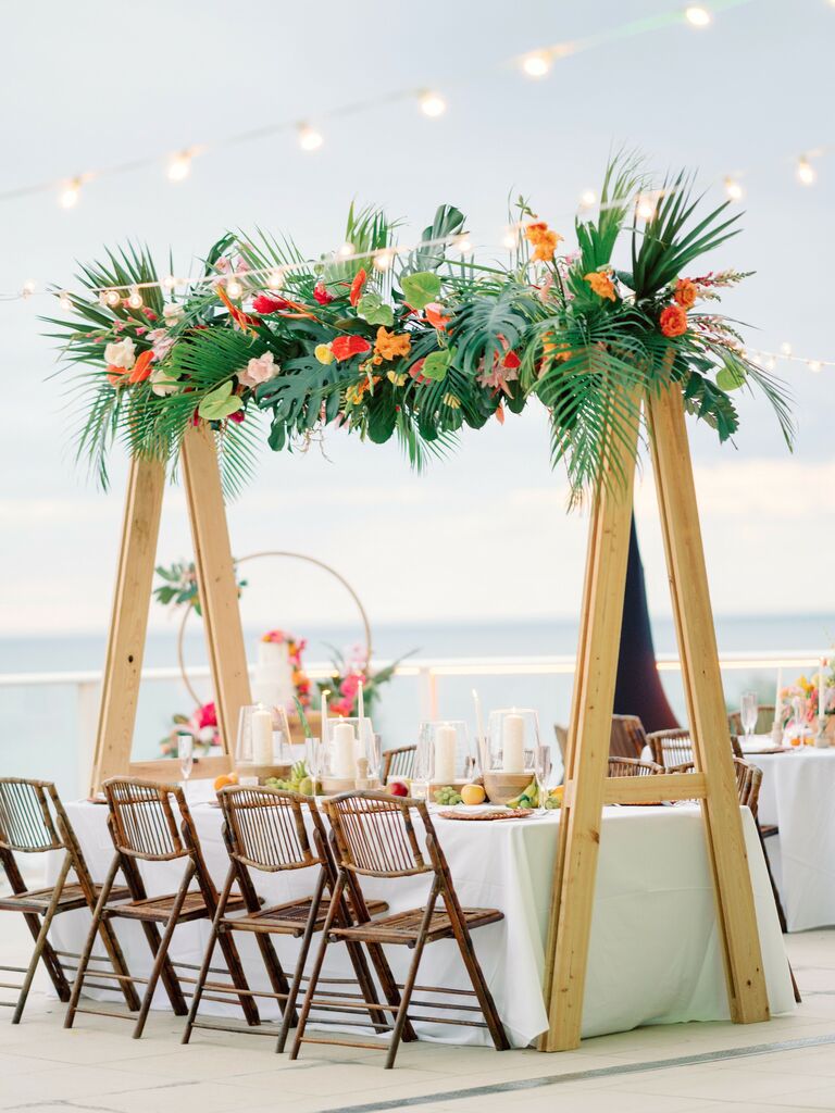 tropical wedding flower installation on wooden A-frame above rectangular reception table