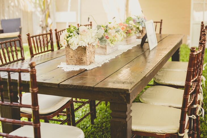 “Our furniture had so much character that I didn’t want to clutter them with huge centerpieces,” Roxy says. Instead, they highlighted each wooden table with classic ivory lace runners and low centerpieces. The tablescapes were filled with wooden breakaway boxes of ivory roses, white hydrangeas, green hypericum and pink garden roses from Flowers International Events.