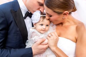 Groom in Navy Tux and Bride in Classic Wedding Gown Kiss Baby Daughter