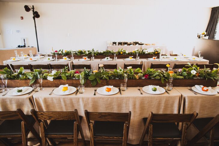 The reception took place inside Ace Hotel & Swim Club in Palm Springs, California, with family-style dining tables dressed in burlap linens. The table was set with white dinnerware decorated with fresh fruit on top. The middle of the dining tables were decorated with long wooden boxes filled with lush arrangements of plants and flowers.