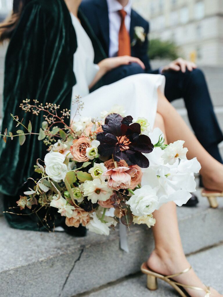 Bride holding fall wedding bouquet with white, pink and dark purple flowers