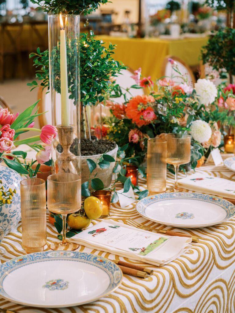 colorful wedding tablescape with potted topiaries, patterned blue plates, yellow textured tablecloth, lemons and pink tulip centerpieces