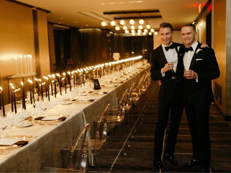 grooms smiling and standing beside table with black taper candles
