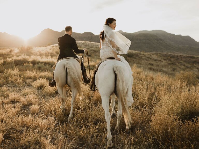 Newlyweds ride horses through a beautiful natural scene. 