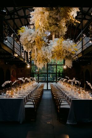 Dim-Lit, Modern Reception Space With Soft Yellow Lights, Flowers, Orchids on Tables and Floating Floral Installation Overhead