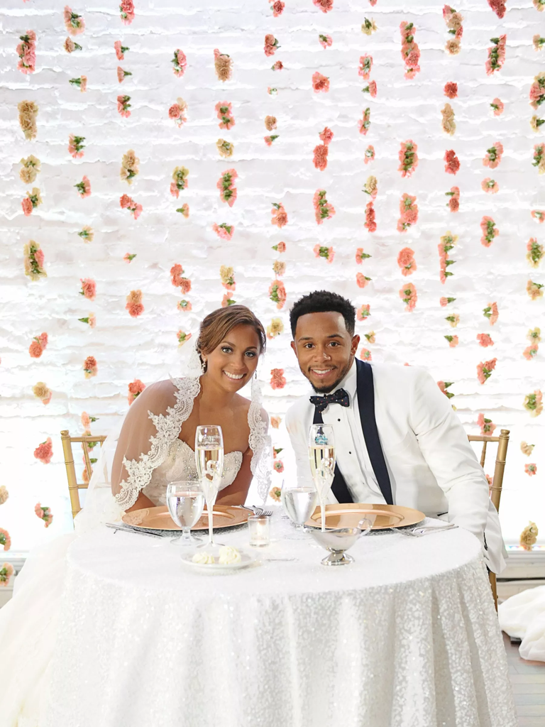 Bride and groom smiling in front of carnation flower wall.