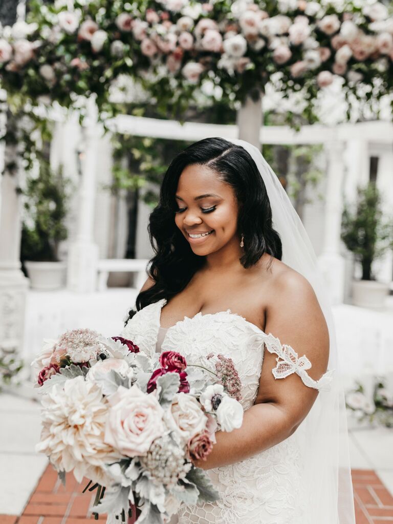 Bride holds a bouquet of white and pink dahlias and roses. 