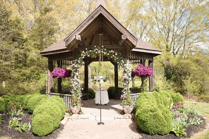 Pratt Gardens’s wooden gazebo was covered in flowers for their ceremony in Pilesgrove, New Jersey. Fuchsia petunias were hung along the sides, while this lush wedding arch covered the front. The arrangement was filled with eucalyptus, pink roses, white tulips, coral carnations, greenery and pink hydrangeas.