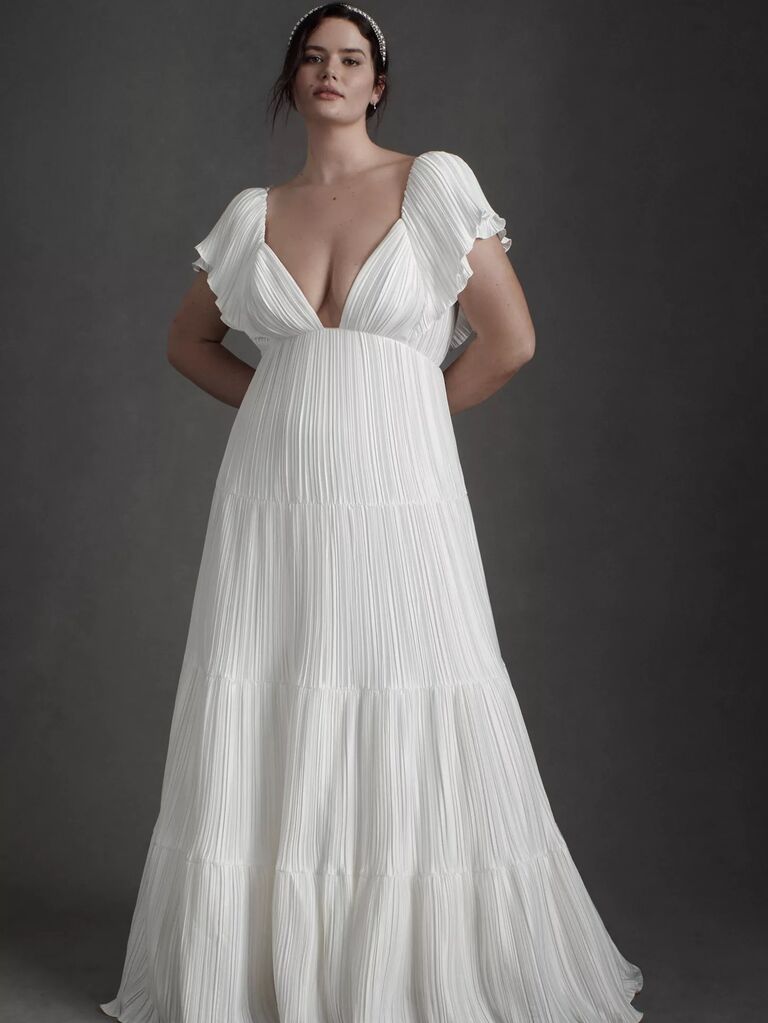 Model wears a white gown with a plunging neckline and fluttering sleeves. 