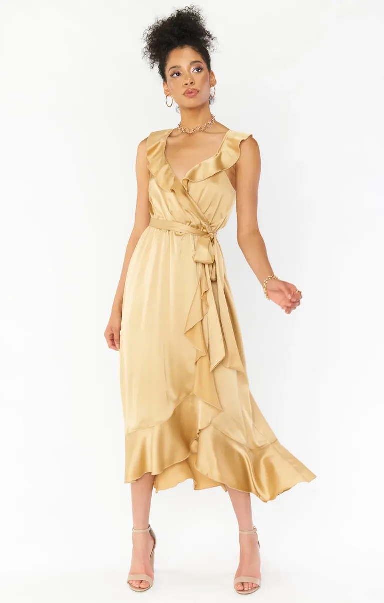 Model wears a golden silk dress with ruffled detailing and a tied waist. 
