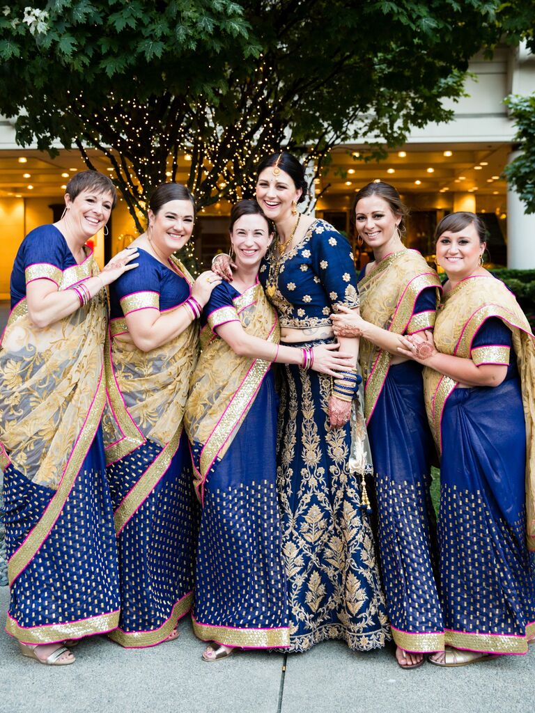 Bridesmaids dressed in navy blue and gold saris with pink highlights.