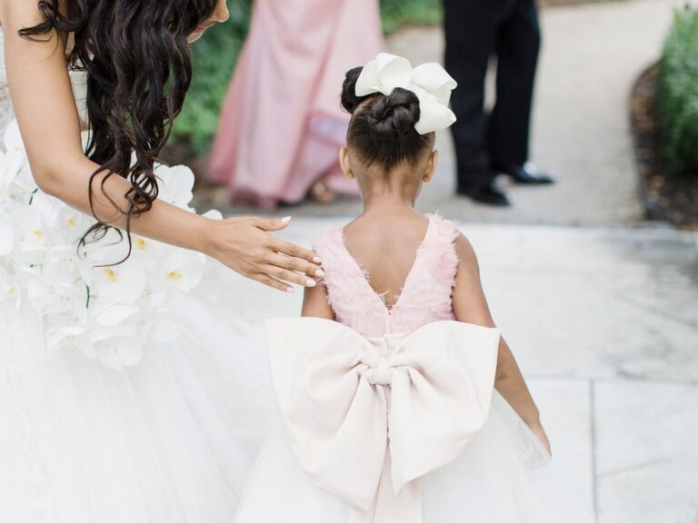 Flower girl wears her hair in an updo with a large white bow. 
