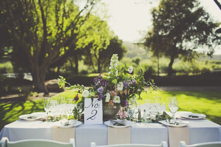 Overgrown floral centerpieces, classic calligraphed table numbers and a makeshift table runner of eucalyptus leaves perfectly fit the vineyard venue.