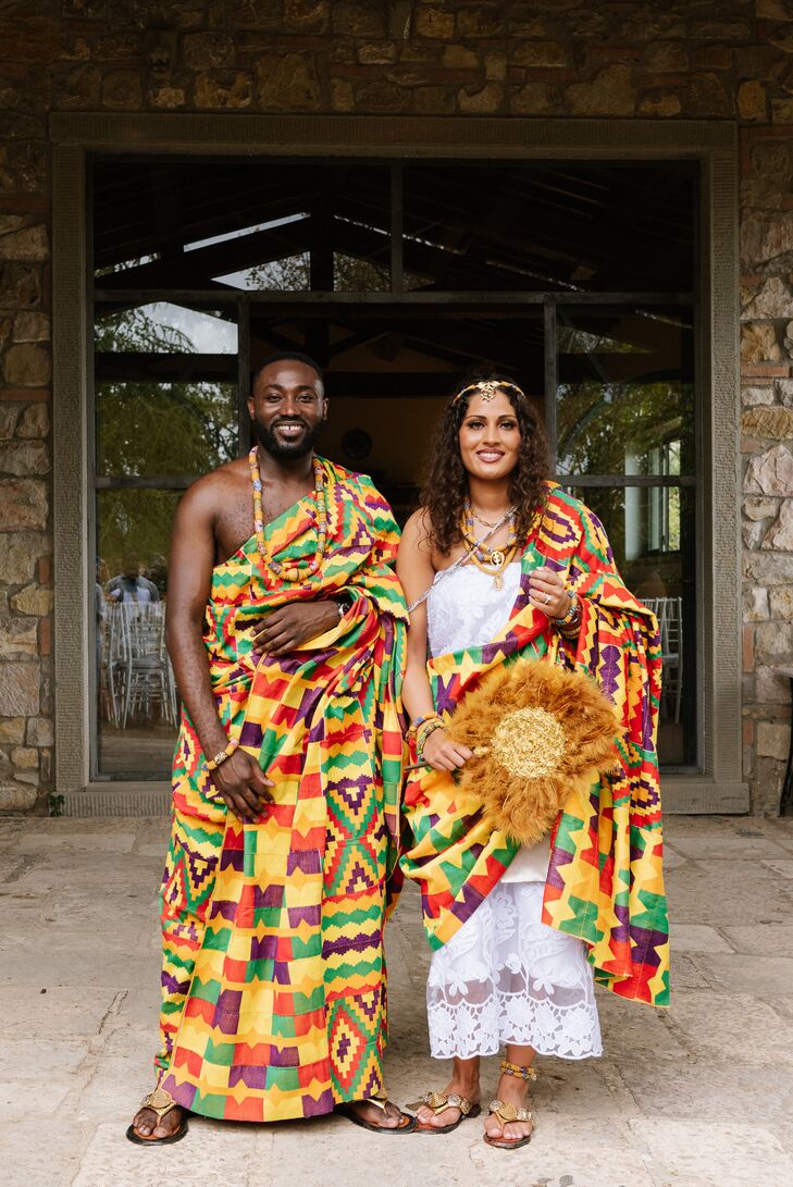 A groom and bride in traditional, colorful Ghanaian Kente featuring yellow, red, green and purple, as well as a headpiece and necklaces, for a multicultural wedding featuring customs from Ghana, India, and Europe.