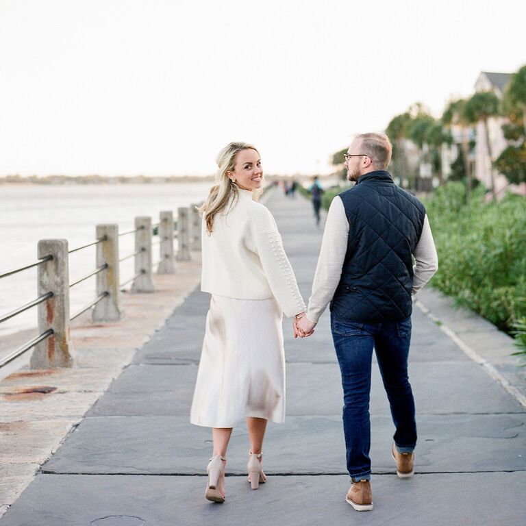 Couple holding hands and walking on sidewalk by water in South Carolina