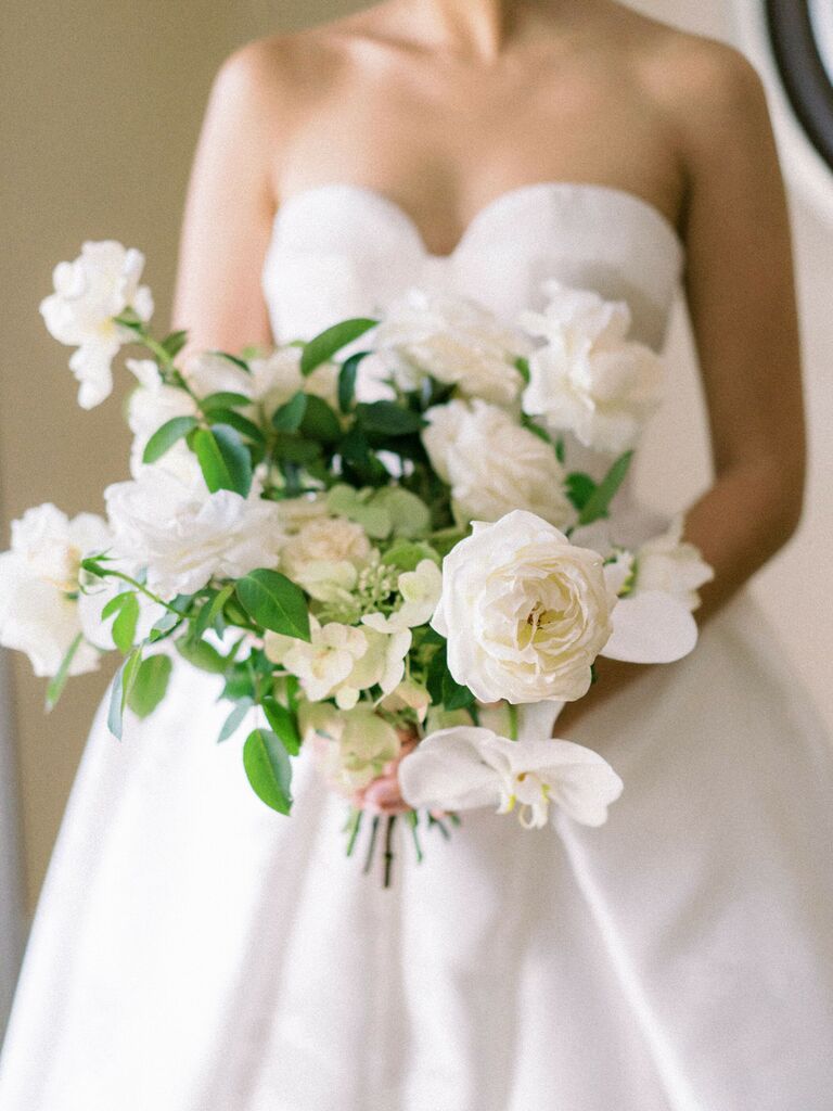 bride holding classic garden style wedding bouquet with white roses and greenery