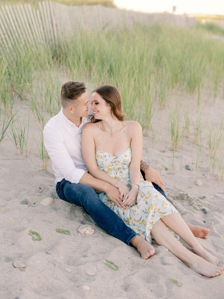 Couple cuddles in the sand on the beach. 