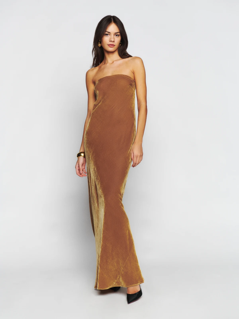 A model wears a strapless floor-length wedding guest dress in a metallic tone.