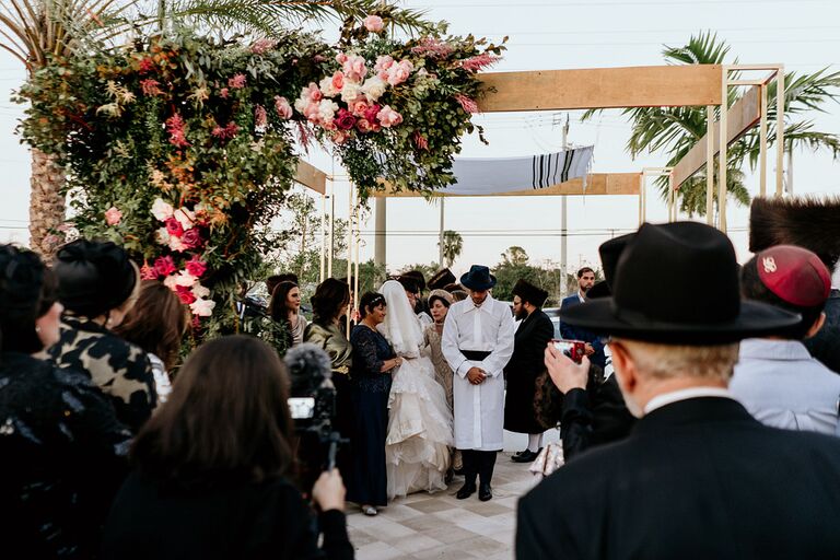 Couple and wedding guests huddled together under chuppah.