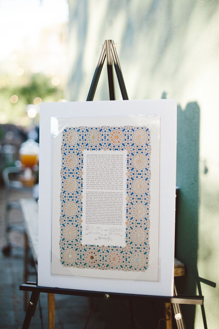 Emily and Chris signed the ketubah before their outdoor ceremony, making them officially married. The ketubah was bordered by a brown-and-blue-tiled pattern that was encased in a white frame, which was on display for the rest of the day.