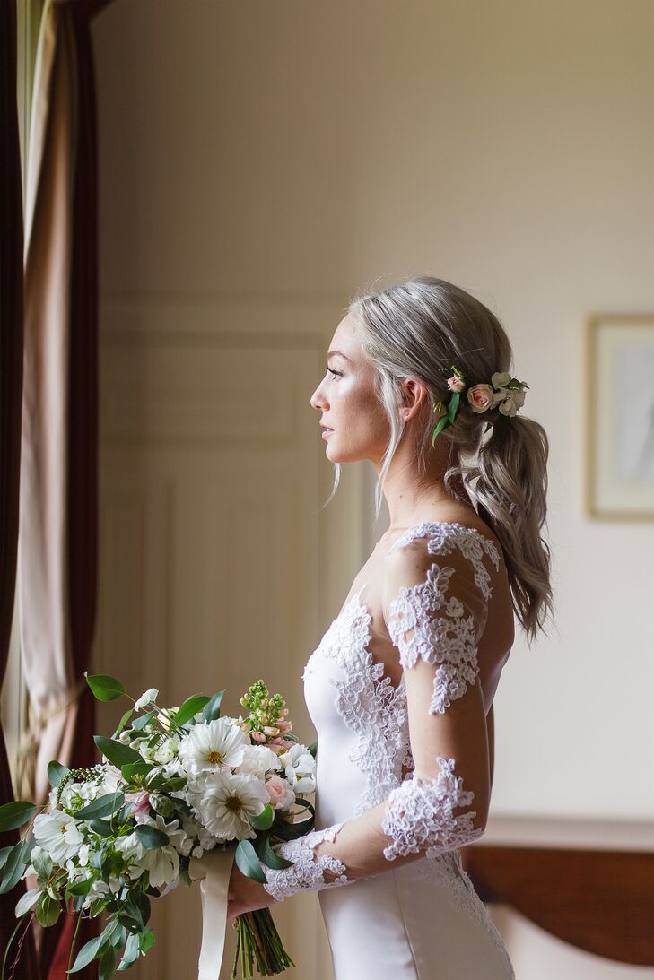 Bringing a bohemian quality to her modern, romantic wedding gown, Elizabeth wore her hair in a low ponytail. Loose, face-framing tendrils and elegantly undone waves lent a softness to her look. A cluster of small pink and cream-colored roses were added at the base of the ponytail, capturing the essence of the Irish countryside and the beauty of the garden where the ceremony took place.