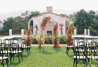 outdoor wedding ceremony with triple wooden arch backdrop decorated with pink bougainvillea flowers
