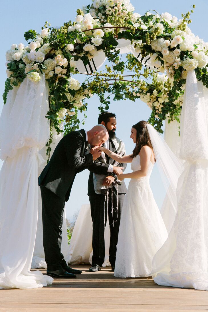 Alyssa and Alex got married under a chuppah adorned with ivory blooms and greenery at the top, and thick white sheets covering the sides.