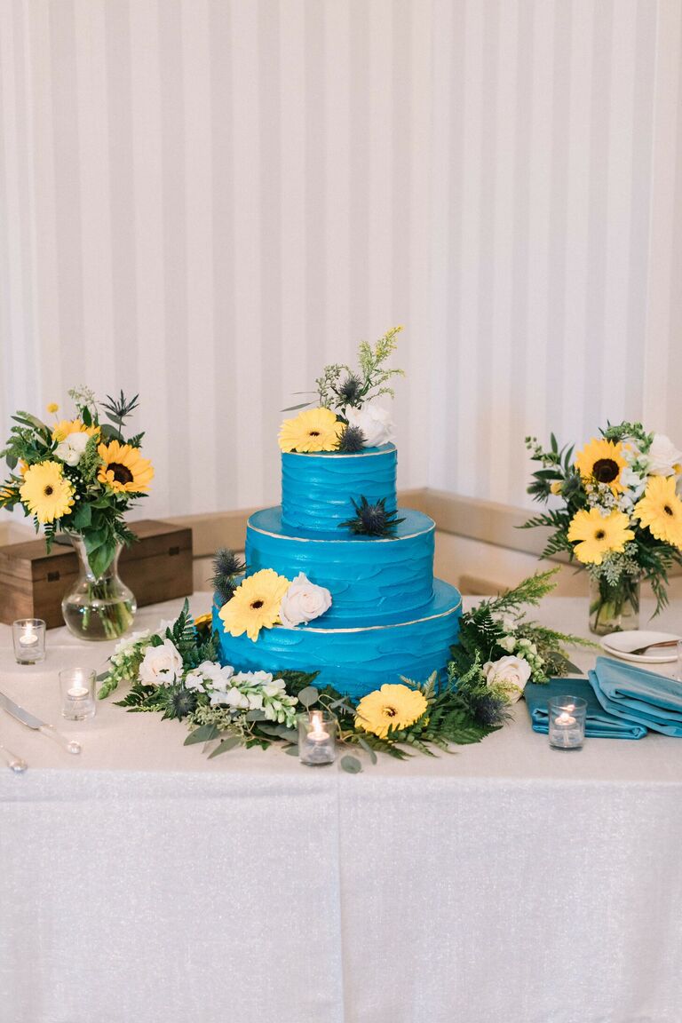 Bright blue cake decorated with yellow daisies and sunflowers