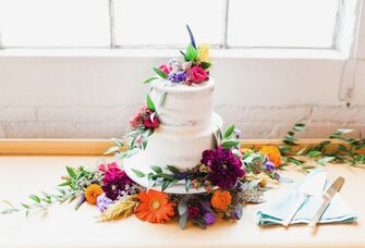 two tier buttercream wedding cake decorated with colorful purple, red and yellow flowers