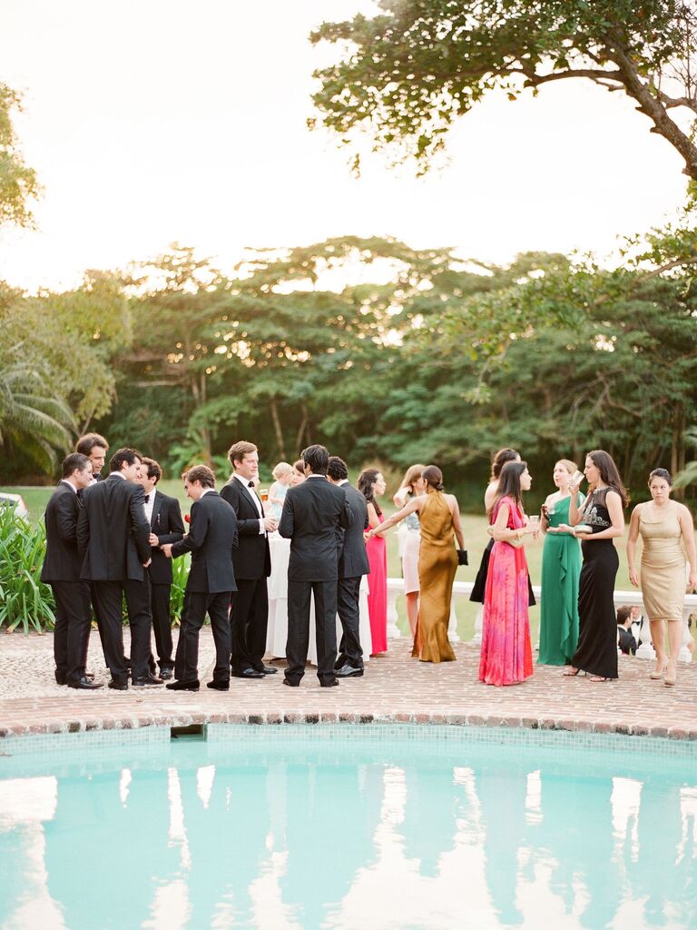 wedding guests mingling and drinking cocktails at outdoor wedding venue with pool