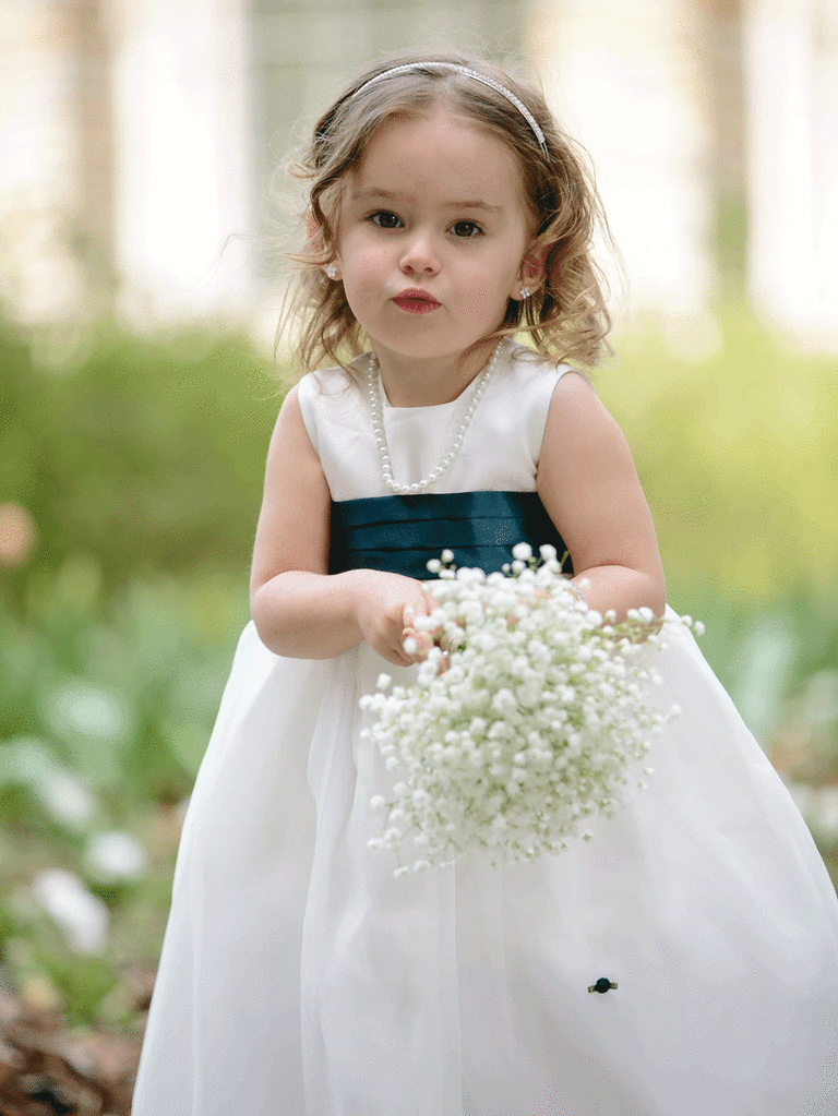 Flower girl in white flower girl outfit holding baby's breath.