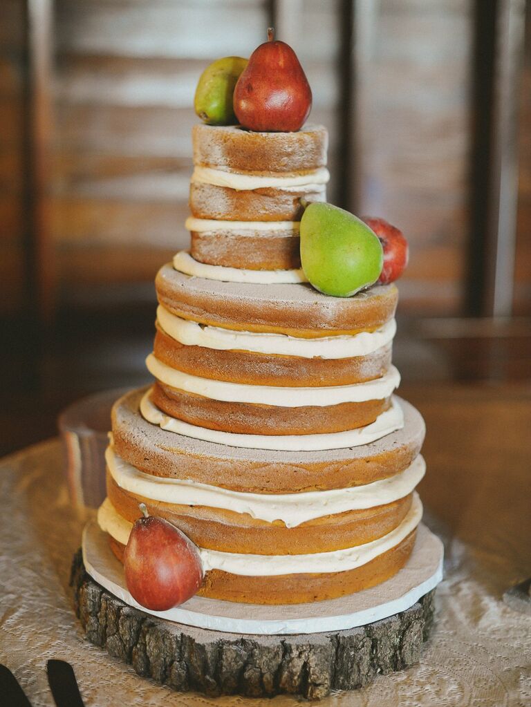 three tier naked wedding cake on wooden cake stand decorated with red and green pears
