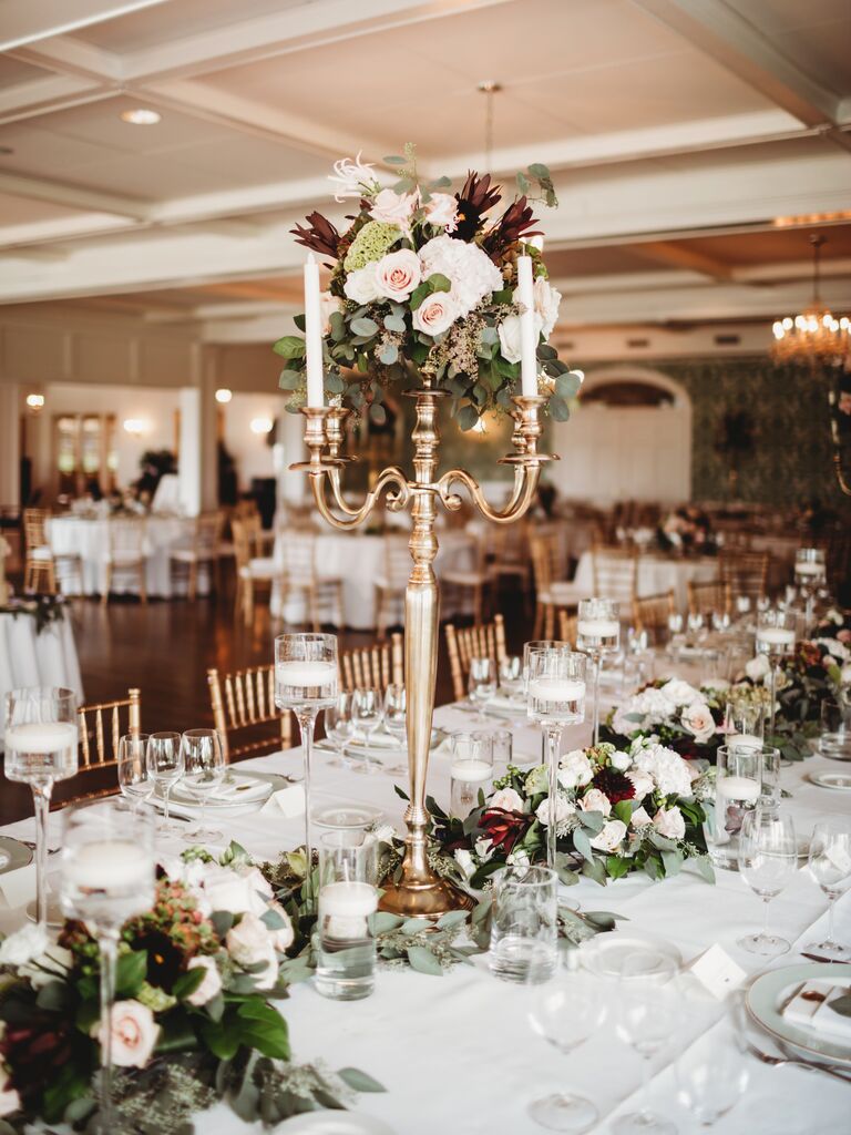 tall wedding centerpiece with gold candelabra, white candles and burgundy and blush flowers