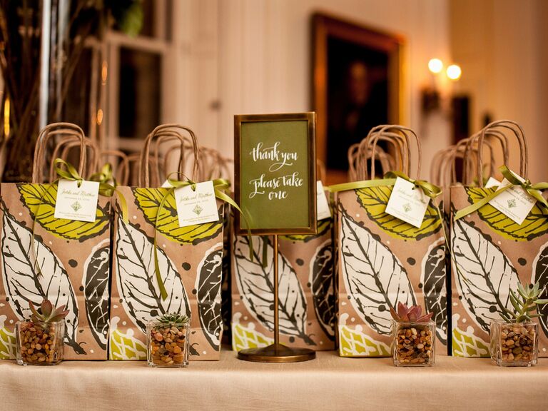 Wedding party favors in brown bags with green leaf illustrations.