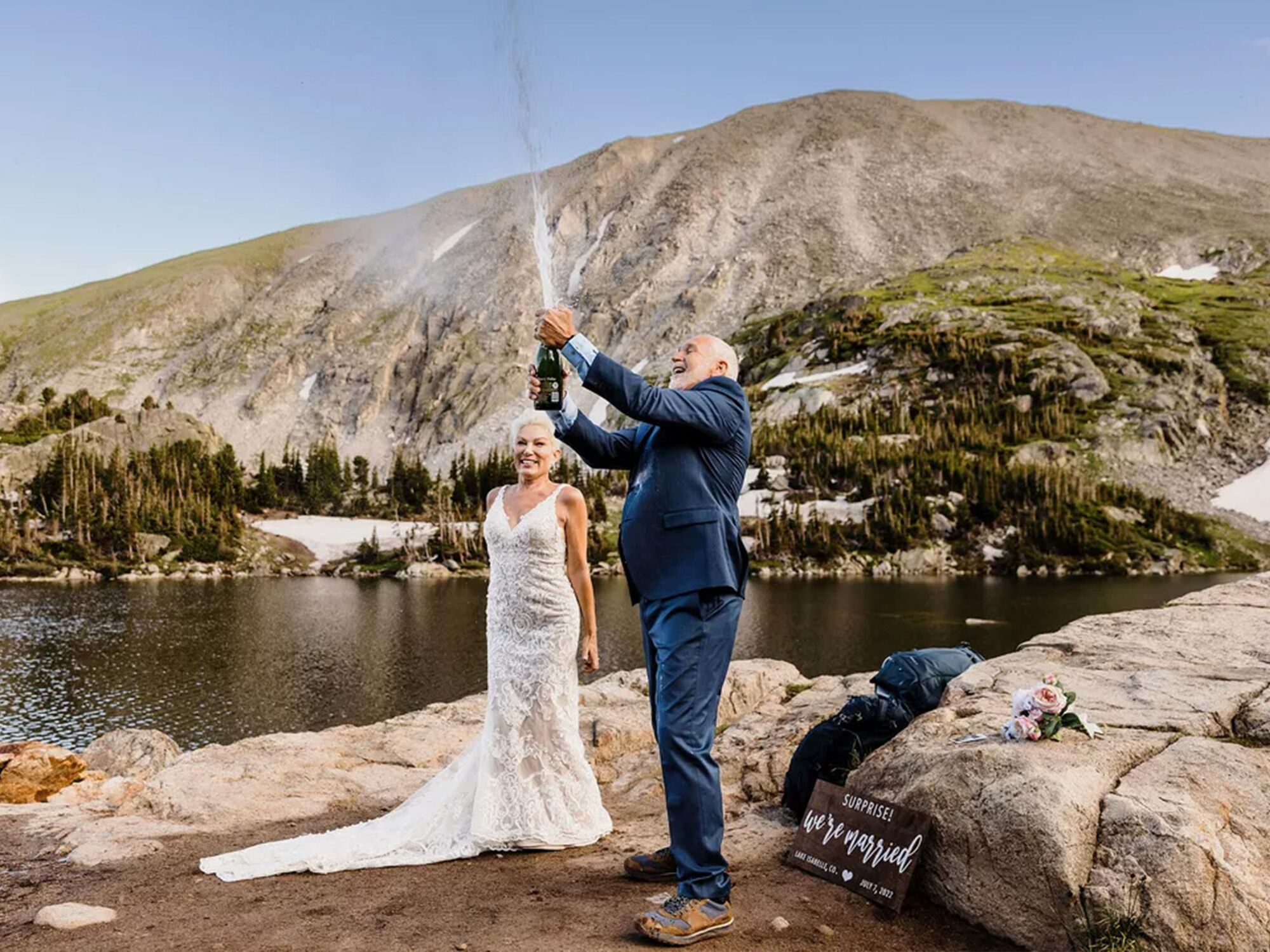 Married couple popping champagne by a lake