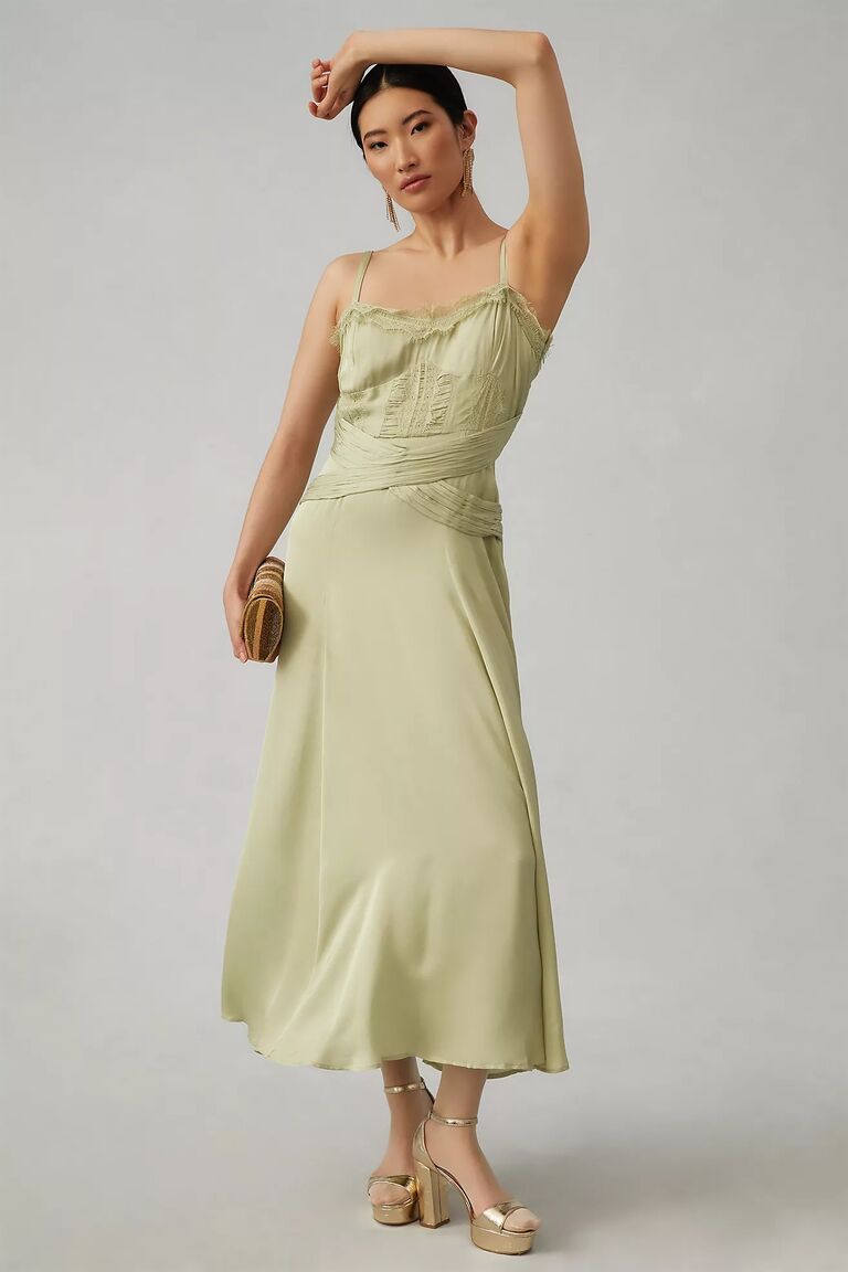 Model wears a sage green dress with lace detailing. 