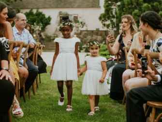 Flower girls wearing white holding hands walking down the aisle