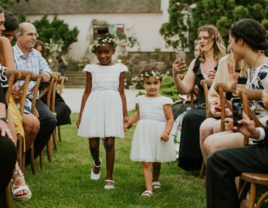 Flower girls wearing white holding hands walking down the aisle