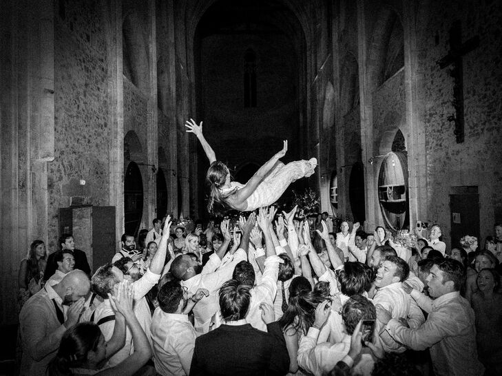 Black-and-White Photo of Guests Throwing Bride Up in Air at Lively Reception in France
