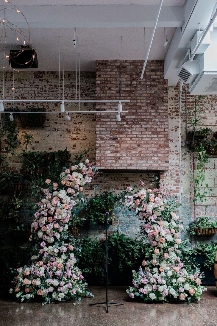 Asymmetrical Floral Ceremony Arch Against Ivy-Laden Exposed Brick Wall