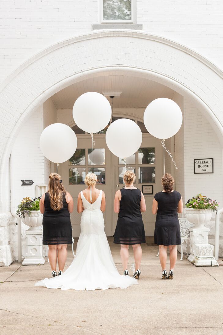 The bride and her bridesmaids stood holding the strings of large white balloons. The bridesmaids wore knee-length black cocktail dresses with black-and-white-striped shoes, which matched the wedding day's classic color palette.