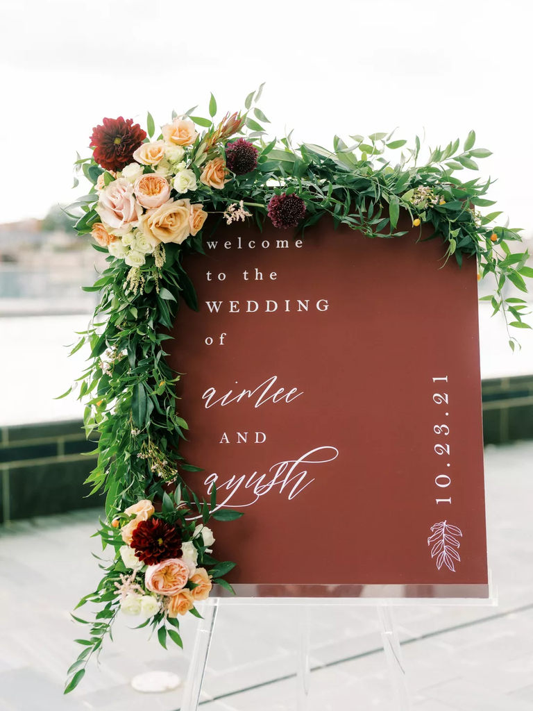 A gorgeous clear easel holds a welcome sign, adorned with roses.